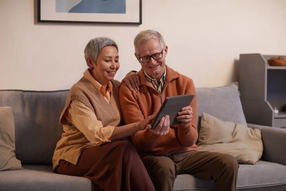 Casal sentado no sofá da sala consultando um tablet juntos, num ambiente claro